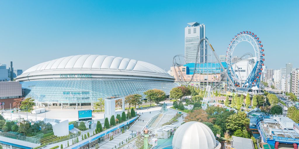 東京ドームシティの写真。左側に東京ドーム。右奥側に観覧車やジェットコースターなどの遊園地が広がっている。